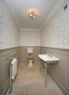 a bathroom with a toilet, sink and radiator next to a wallpapered wall