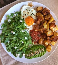 a white plate topped with potatoes, spinach and an egg on top of it