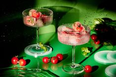 two glasses filled with food sitting on top of a green countertop next to tomatoes and cucumbers