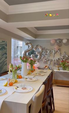 the table is set with plates, silver balloons and flowers in vases on it