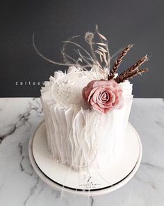 a white cake with pink flowers and feathers on the top is sitting on a marble table