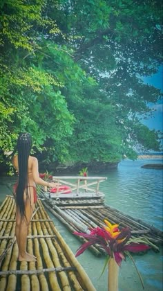 a woman standing on top of a bamboo raft in the water next to a forest