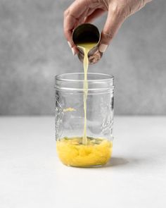 someone pouring orange juice into a glass jar