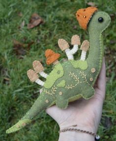 a hand holding a stuffed toy dinosaur in the grass