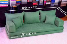 a green couch sitting on top of a pink rug next to a pile of pillows