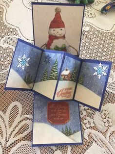 three cards with snowmen on them sitting on a lace tablecloth covered table cloth