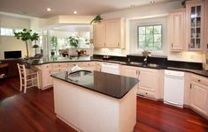 a large kitchen with white cabinets and black counter tops, hardwood flooring, and an island in the middle