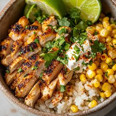 a bowl filled with chicken, rice and corn on top of a table next to a lime wedge