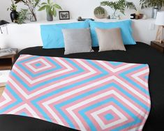 a bed covered in pink and blue pillows next to potted plants on the wall