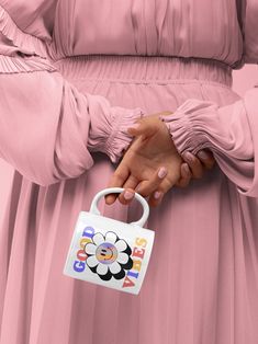 a woman in a pink dress holding onto a small bag with flowers on it's handle