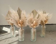 three glass vases with dried flowers in them