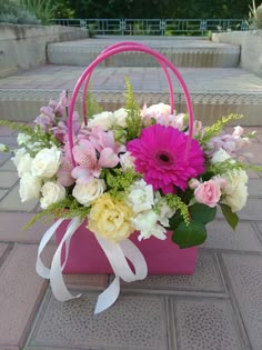 a pink basket filled with lots of flowers on top of a brick floor next to steps