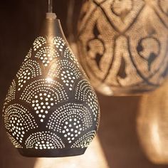 two lamps hanging from the ceiling with white and black designs on them, one has a light bulb that is turned on