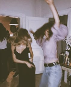 two women are dancing in a room with other people