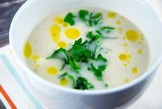 a white bowl filled with soup sitting on top of a striped table cloth next to a spoon