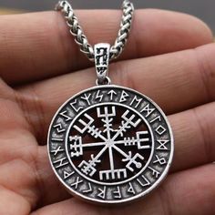 a person is holding a silver pendant with symbols on it