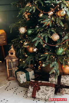 a christmas tree with presents under it in front of a small wooden box and lantern