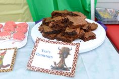 a table topped with brownies and cookies on top of white plates covered in frosting