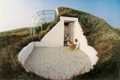 two people sitting on the ground in front of a house with grass growing on it