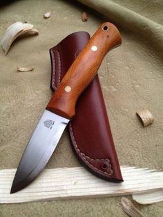 a knife with a brown leather sheath sitting on top of a piece of wood