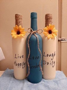 three bottles with words written on them and sunflowers tied to the top one