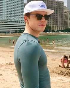 a man standing on top of a sandy beach next to the ocean with buildings in the background