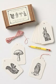 four tags with animals and mushrooms on them next to a box of yarn, pencil and thread