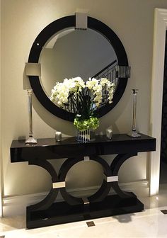 a black console table with flowers and candles on it in front of a round mirror