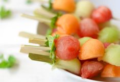 there are many different fruits on the skewers in this white bowl with green garnish