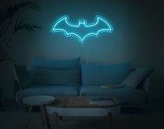 a living room with a couch and a neon batman sign on the wall above it