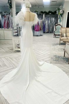 a white wedding dress on display in a room with other dresses and accessories behind it