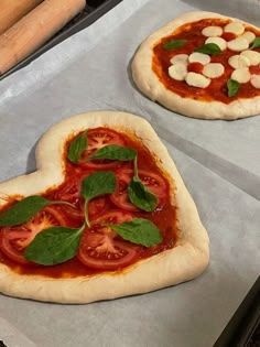 two uncooked pizzas with tomatoes and basil on them