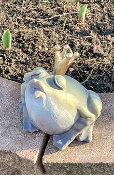 a statue of an elephant laying on top of a cement block next to flowers and dirt