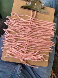 a clipboard with pink yarn on it and a person's feet in jeans