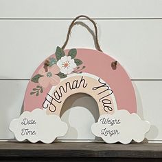 a wooden sign with flowers and clouds hanging from it's sides on a shelf