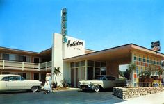 two cars parked in front of a motel with a woman standing next to the entrance