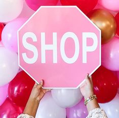 two hands holding up a pink stop sign surrounded by balloons