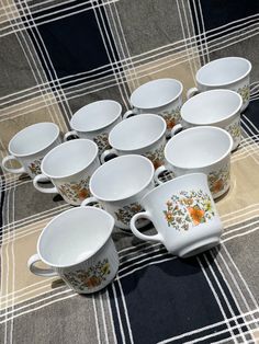 a table topped with lots of cups and saucers on top of a checkered cloth