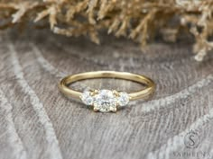 a three stone diamond ring sitting on top of a piece of fabric next to a tree branch