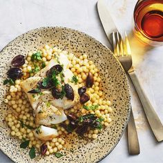 a white plate topped with fish and corn next to a glass of wine on top of a table