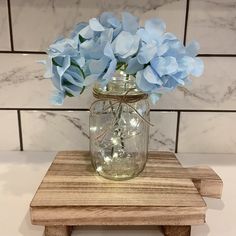 a mason jar filled with blue flowers sitting on top of a wooden table next to a tile wall