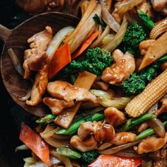 stir fry with chicken, broccoli, carrots and corn in a wooden spoon