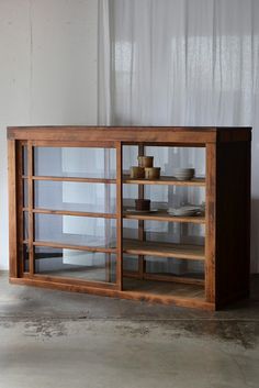 a wooden cabinet with glass doors and shelves on the front, against a white wall