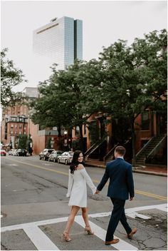 an engaged couple walking across the street holding hands