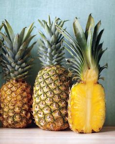 three pineapples with one cut in half and the other whole on a table