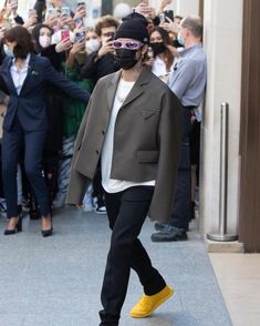 a man wearing a face mask walks down the street in front of a group of people