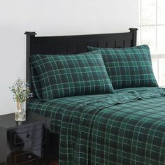 a bed with green plaid sheets and pillows in a room next to a black dresser