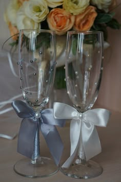 two wine glasses with bows on them sitting next to each other in front of a bouquet of flowers