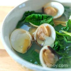 a white bowl filled with broccoli and clams on top of a wooden table