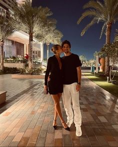 a man and woman posing for a photo in front of some palm trees at night